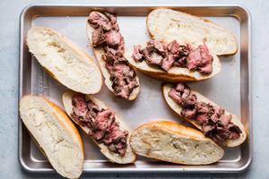 homemade french dip sandwiches open face on a baking sheet with thinly sliced steak and garlic butter