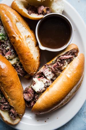 the best french dip sandwiches on a serving plater with thinly sliced steak, garlic butter, swiss cheese and au jus sauce