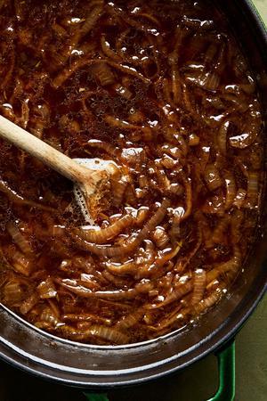 beef stock, wine, butter, nutmeg, thyme, bay leaf, garlic, salt, pepper and caramelized onions being stirred in a pot