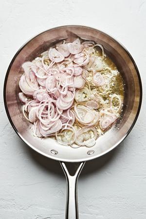 sliced raw shallots being fried in vegetable oil in a skillet