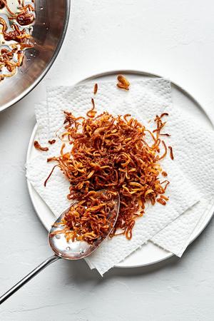 Fried shallots being transferred from a hot skillet with a slotted spoon onto a paper towel lined plate