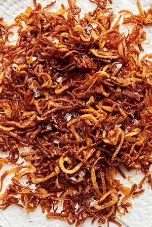 homemade fried shallots draining on a paper towel lined plate seasoned with salt