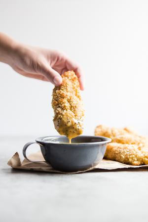hand dipping baked chicken tender into honey mustard sauce