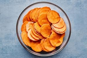 sweet potatoes being tossed with coconut oil, cinnamon, nutmeg, and salt