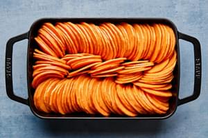 sweet potatoes tossed with coconut oil, cinnamon, nutmeg, and salt being arranged in a baking dish