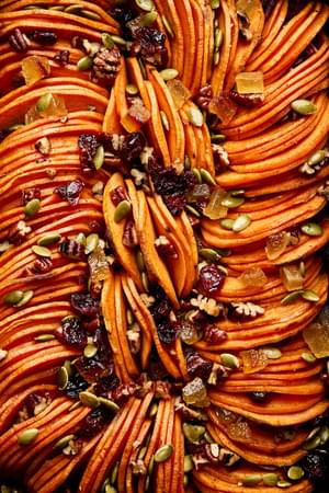 healthy sweet potato casserole topped with pumpkin seeds, candied ginger, dried cranberries & chopped pecans