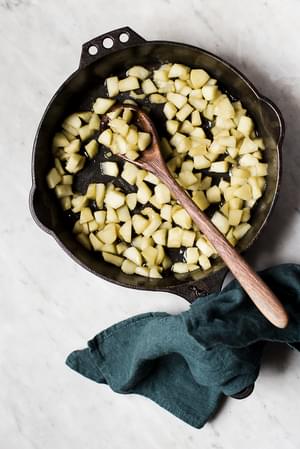 chopped apples sautéed in a pan with a wooden spoon