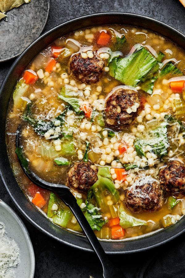Italian wedding soup in a bowl with a spoon toped with parsley and Parmesan