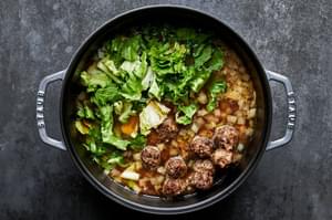 meatballs, escarole, and veggies being cooked in chicken and beef broth for italian wedding soup