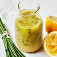 homemade lemon vinaigrette in a glass dressing bottle next to chive and a sliced lemon