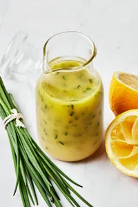 homemade lemon vinaigrette in a glass dressing bottle next to chive and a sliced lemon