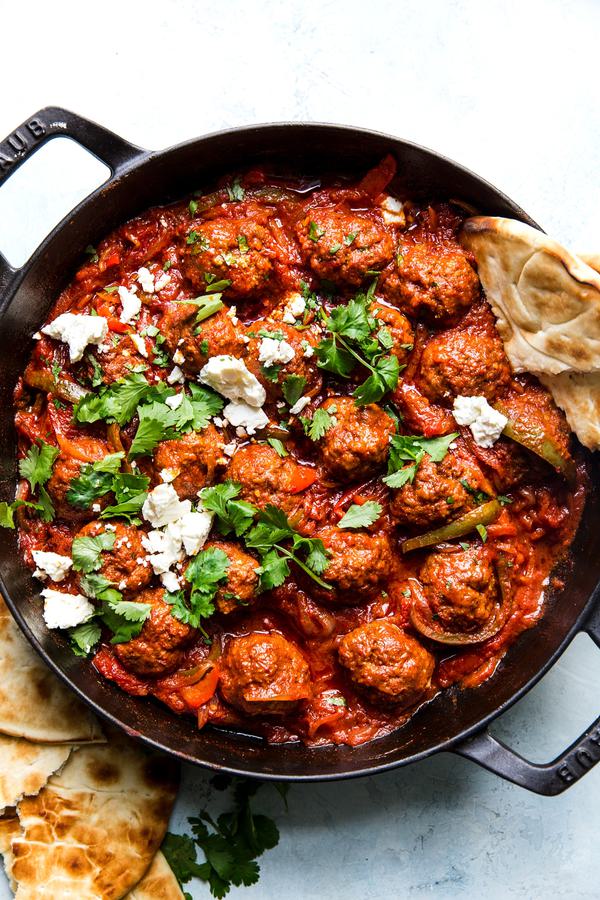 spiced meatballs simmered in a shakshuka sauce in a skillet served with feta, parsley and pita bread