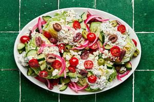 a platter of mediterranean wedge salads with tomatoes, cucumber, greek olives, pickled red onions and creamy feta dressing