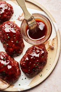 homemade mini meatloafs on a serving platter being brushed with a brown sugar sauce