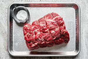 a raw roast being seasoned with salt