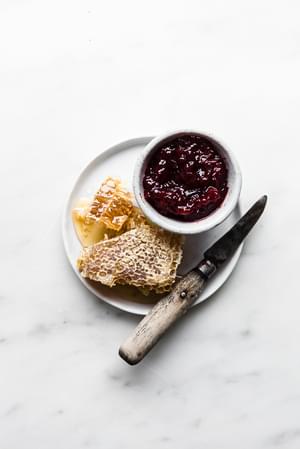 a plate with honey comb, a small knife and a small bowl of jam.