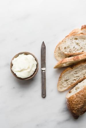 a small bowl of butter next to a butter knife and slices of crusty bread