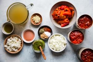 ingredients laid out for roasted red pepper soup, stock, onions, pesto, goat cheese, olive oil, fire roasted tomatoes, spices