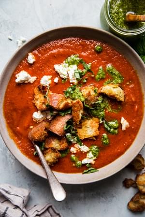 Roasted red pepper soup in a bowl with croutons, goat cheese and pesto with a spoon