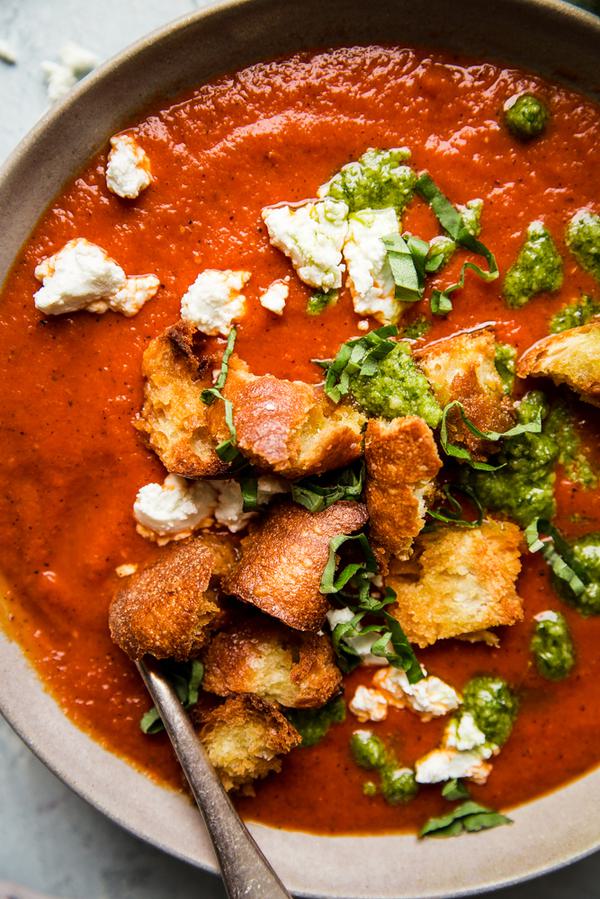 Roasted red pepper soup in a bowl with croutons, goat cheese and pesto with a spoon