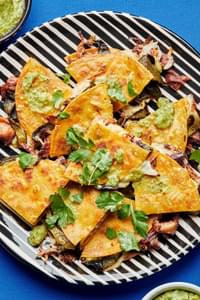 Roasted poblano and carnitas quesadillas cut in quarters on a serving platter topped with salsa verde and cilantro
