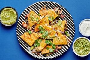 Roasted poblano and carnitas quesadillas on a serving platter served with bowls of guacamole, sour cream & salsa verde