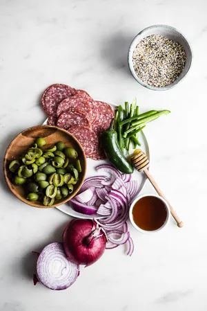 ingredients laid out for Salami, Jalapeño & Olive Pizza with Honey, red onion