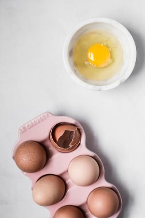 6 eggs in a pink ceramic cartoon and one egg cracked in a small bowl