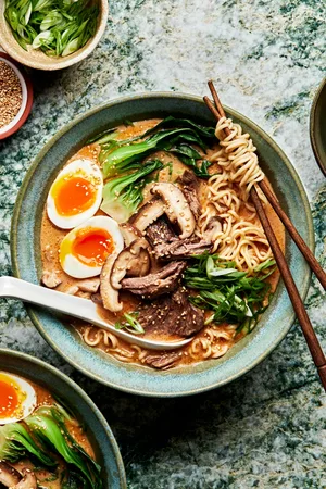 a bowl of slow cooker curry beef ramen topped with soft boiled eggs with a spoon and chopsticks