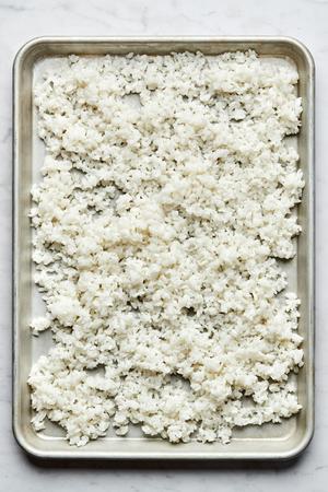 homemade sushi rice made with salt, sugar and unseasoned rice vinegar spread out on a baking sheet to cool