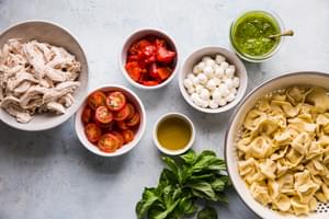 a bowl of chicken, cooked tortellini, basil, mozzarella, pesto olive oil, tomatoes