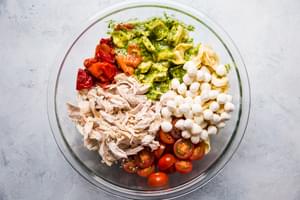 a large mixing bowl with tortellini, pesto, mozzarella, roasted red bell peppers, cherry tomatoes and shredded chicken