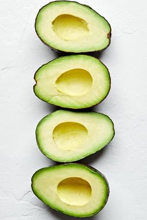 2 ripe avocados cut in half with the pits removed lined up on the counter