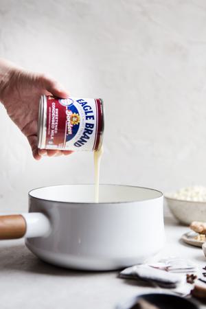 hand pouring sweetened condensed milk into a sauce pan