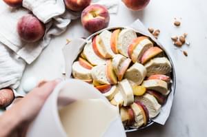 hand pouring milk and cream into peach and almond bread pudding