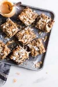 Coconut Pecan Caramel Bars on a baking tray with caramel sauce in a jar