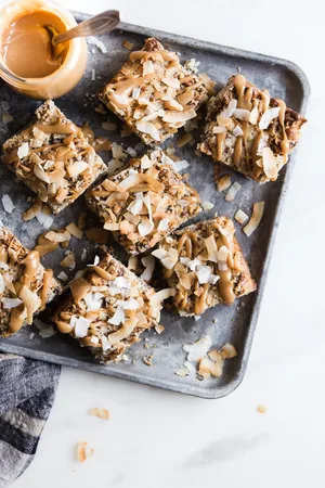 Coconut Pecan Caramel Bars on a baking tray with caramel sauce in a jar