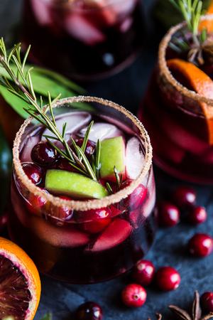 3 glasses filled with red sangria made with cranberries, apples, oranges and brandy with a cinnamon sugar rim.