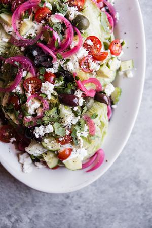Mediterranean Wedge salad with pickled onions, olives feta dressing and cucumbers and tomatoes on a plate