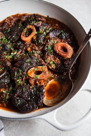 homemade osso buco cross cut beef shanks in a braiser with sauce and a serving spoon