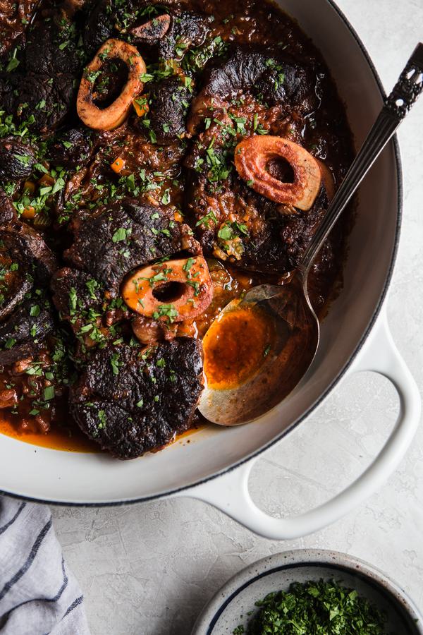 Osso buco, cross cut shanks with fresh parsley and garlic in a braiser with serving spoon.