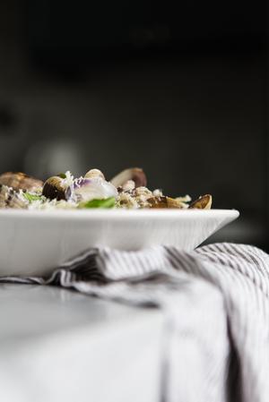 a bowl of Steamed Clams With Linguini a loaf of bread with a linen