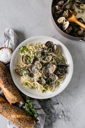 a bowl of Steamed Clams With Linguini a loaf of bread with a linen