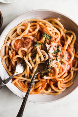 Three Ingredient Tomato Sauce with noodles in a bowl with fresh basil and parmesan cheese and two forks swirled in the pasta