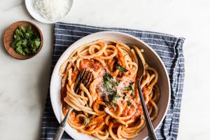 Three Ingredient pomodoro sauce with noodles in a bowl with fresh basil and parmesan cheese and two forks swirled in pasta