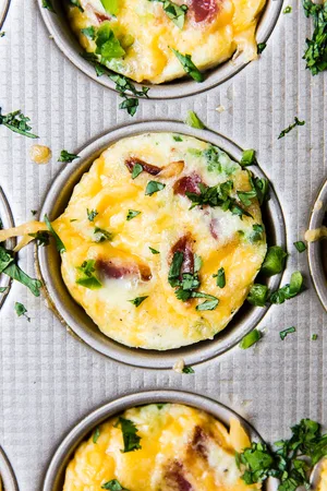 close up on one bacon cheddar egg cup in a muffin tin garnished with cilantro