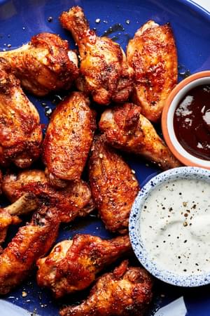 Homemade baked chicken wings on a plate served with ranch dressing and bbq sauce in small bowls