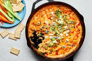 homemade buffalo chicken dip in a cast iron skillet next to carrots, celery and chicken cracker for dipping