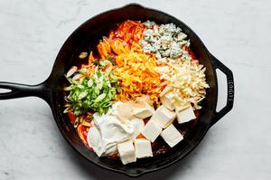 chicken, buffalo sauce, cream cheese, sour cream, cheddar, mozzarella, blue cheese, spices and green onions in a skillet