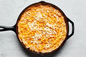 homemade buffalo chicken dip in a cast iron skillet sprinkled with cheddar and mozzarella cheese on top ready for the oven